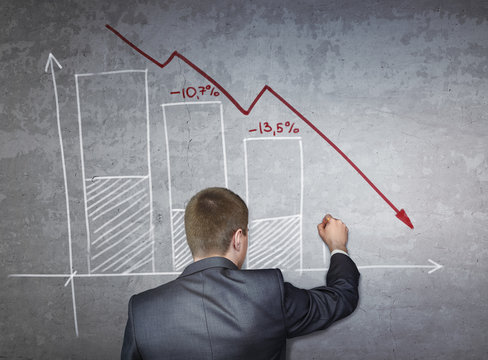 Businessman draws on concrete wall financial and stock charts. Business, falling markets concept