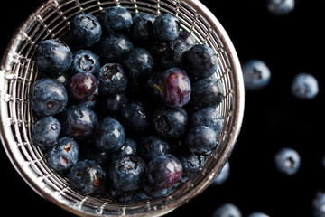 Blueberries in steel cup strainer on black background from above