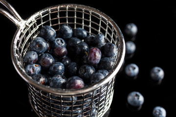 Blueberries in steel cup strainer on black background from side high angle