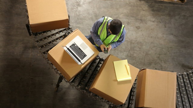 Man in shipping warehouse uses laptop, overhead view