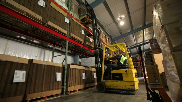 Worker in warehouse moves inventory with forklift