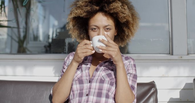 Young woman holding cup of coffee while sitting alone on a bench