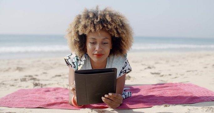 Woman lying on beach towel and using a tablet computer on a beach