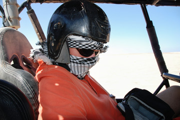 A man in a helmet and face covered sitting in a car in the deser