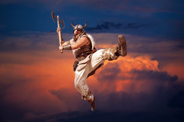 crazy strong viking with traditional costume attacking and jumping from sky in the sunset...