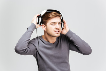 Handsome young man in grey pullover taking off headphones