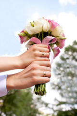 Hands with wedding rings on bridal bouquet