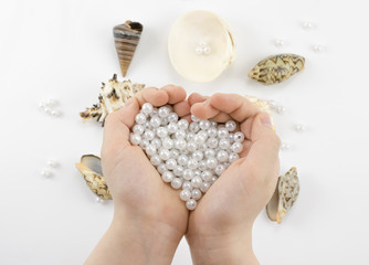 hands with pearl beads and seashells on white background