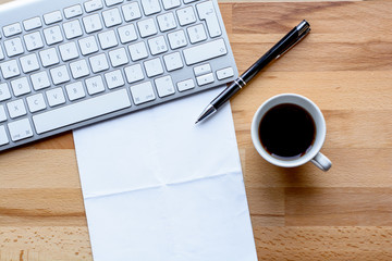 Office desk with keyboard, coffee, pen and paper
