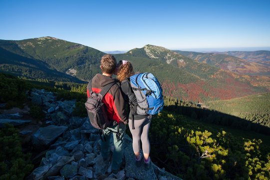 Young backpackers couple kissing at the rocky mountain peak. Enjoying beautiful overview on majestic fall landscape. Warm sunny day.
