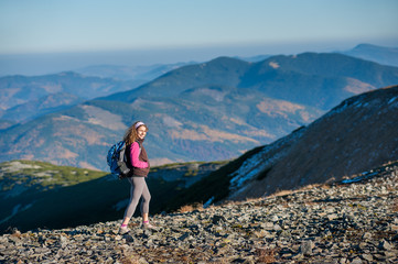 Naklejka na ściany i meble Young happy woman backpacker is walking on mountain ridge with beautiful mountains on background. Sunny autumn day.