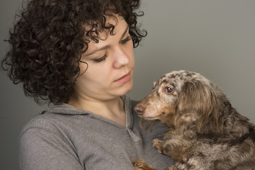 Beautiful young woman with curly brown hair cuddles small dapple dachshund