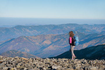 Fototapeta premium Young athletic woman backpacker standing on the ridge of the mountain enjoying the open view on the big mountains. Rear view, sunny autumn day.