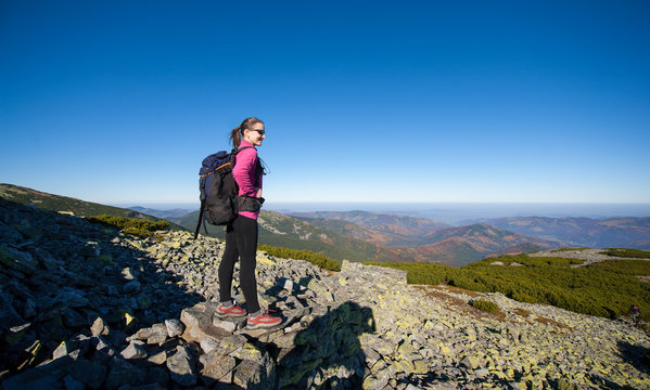 Young woman backpacker standing on rocky mountain peak smiling and looking at beautiful mountain nature landscape. Fall. Copy space