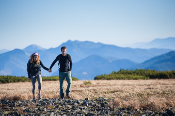 Young couple of tourists hiking in the beautiful mountains on warm sunny fall day. Man and woman holding hands.