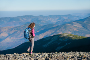 Naklejka premium Young woman tourist is walking on mountain plato with big backpack on. Beautiful mountains on background. Sunny autumn day.
