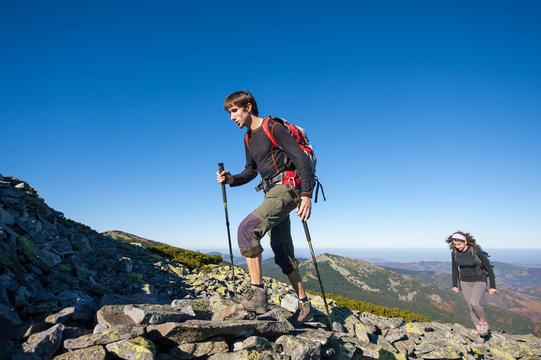 Young hiker couple climbing up rocky the mountain top, high altitude. Beautiful autumn mountain landscape on the background. Fall.