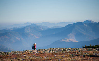 Young girl hiker is walking on mountain plato with beautiful high mountains on background. Sunny autumn day. Ecotourism and healthy lifestyle concept. Copy space