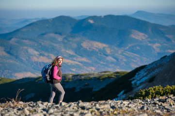 Naklejka na ściany i meble Portrait of young girl hiker is walking on mountain plato with beautiful mountains on background and loooking to the camera. Sunny autumn day.