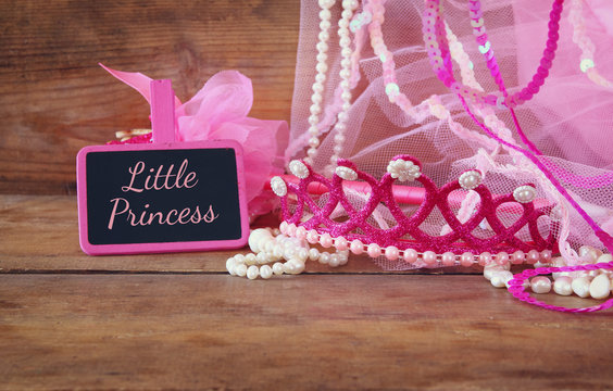 Small girls party outfit: crown and wand flowers next to small chalkboard with phrase LITTLE PRINCESS: on wooden table. bridesmaid or fairy costume. glitter overlay
