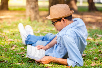 Fototapeta premium Asian young man reading a book on the grass in park