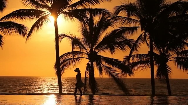 Woman walks by pool at tropical resort, sunset