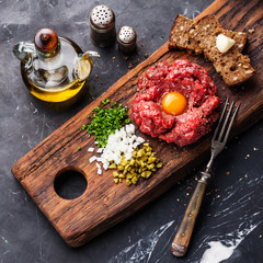 Beef tartare steak with pickled cucumber and onion on dark marbl