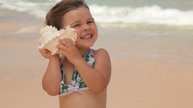 Young girl standing at beach holding shell up to ear