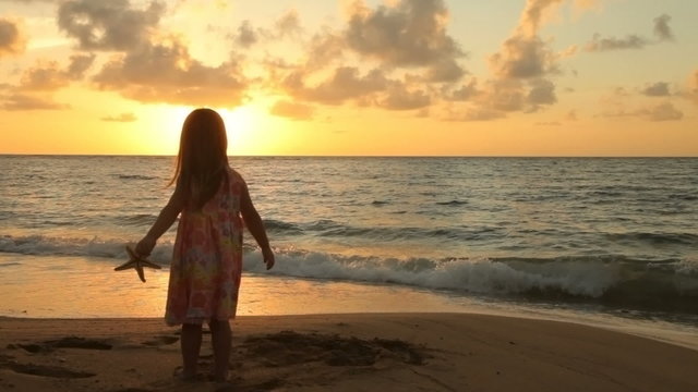 Young girl standing at beach with starfish, sunrise