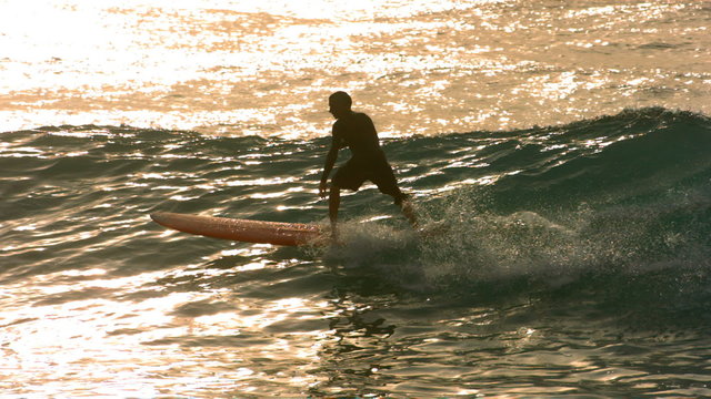 Surfer rides wave in late afternoon light, slow motion