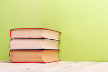 Stack of hardback books, diary on wooden deck table and green background. Back to school. Copy Space. Education background