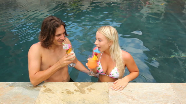 Couple at tropical resort pool, with cocktails