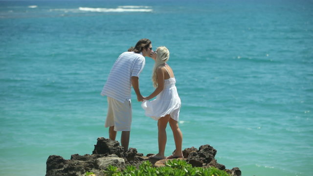 Couple stand on rocks overlooking ocean
