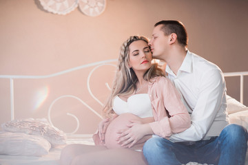 Husband hugging his pregnant wife in white lingerie on a light background, lifestyle, waiting, belly