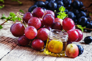 Healing grape seed oil in a glass jar, fresh pink grapes on old