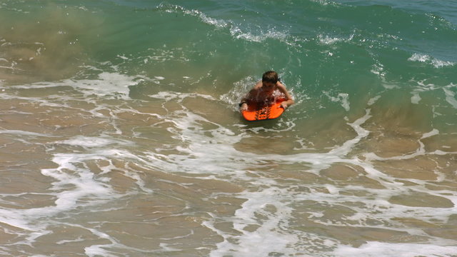 Two young boys boogie boarding in ocean, slow motion