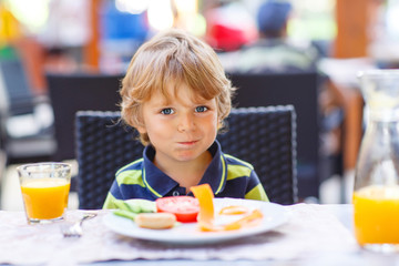 Little kid boy having healthy breakfast in restaurant 