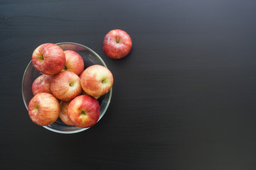 Fototapeta na wymiar Red apple in glass bowl on black wooden desk