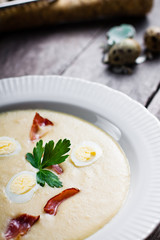 Creamy Horseradish soup with quail egg, black forest ham, decorated with leaf parsley. Soup in a deep plate on a gray wooden table.