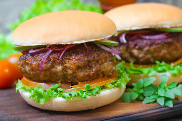Juicy burgers hamburger with a big beef cutlet, tomato, lettuce and onion on wooden background