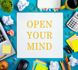 Open your mind. Office table desk with supplies, white blank note pad, cup, pen, pc, crumpled paper, flower on blue background. Top view. Business creative consept.