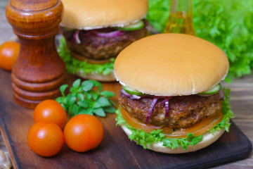 Juicy burgers hamburger with a big beef cutlet, tomato, lettuce and onion on wooden background