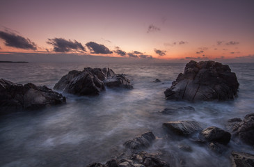 Obraz premium An early morning sunset over rugged rocks in Corneall. A long exposure image of a rocky coastline seascape with waves flowing over hard, dark rocks.