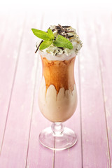 Exclusive coffe cocktail with caramel topping on glass with cream and mint leaf on pink wooden background, frappe