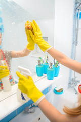 A woman polishing glass using a cleaning sponge and rubber glove