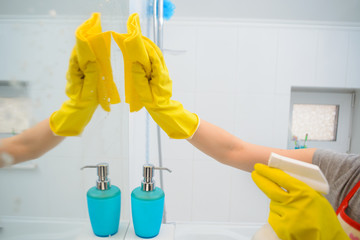 A woman polishing glass using a cleaning sponge and rubber gloves