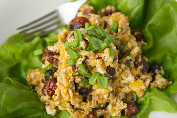 Scrambled eggs with sausage and spring onion on lettuce leaves