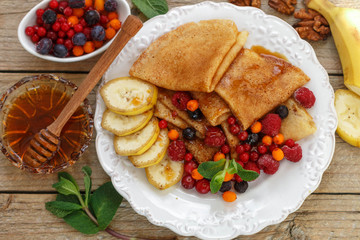 Breakfast. Pancakes with honey and fresh berries - raspberries, cranberries, sea buckthorn and  cowberry. Selective focus

