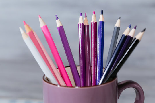 Stack of pink blue and purple colored pencils in a glass on wooden background