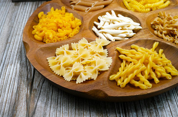 Various mix of pasta and small red tomatoes on wooden bowl
